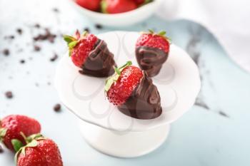 Dessert stand with delicious strawberries dipped in dark chocolate on color background�