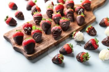 Wooden board with delicious strawberries covered with chocolate on color background�