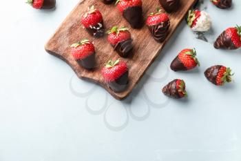 Wooden board with delicious strawberries covered with chocolate on color background�