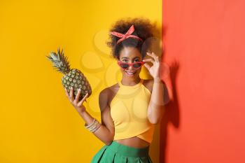 Beautiful African-American woman with pineapple near color wall�