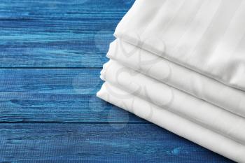 Stack of clean bed sheets on color wooden background�