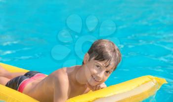Cute boy on inflatable mattress in swimming pool on summer day�
