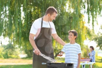 Little boy with his father cooking tasty food on barbecue grill outdoors�
