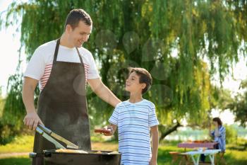 Little boy with his father cooking tasty food on barbecue grill outdoors�