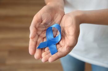 Woman holding blue ribbon, closeup. Cancer concept�