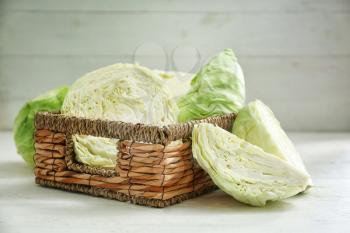 Wicker basket with fresh cabbage on white table�