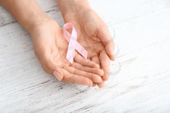 Woman holding pink ribbon on light wooden background. Breast cancer concept�