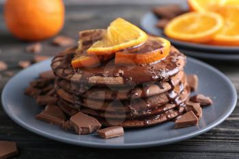 Tasty chocolate pancakes with sweet sauce and sliced orange on plate�