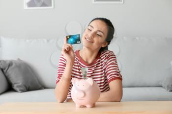 Young woman with piggy bank and credit card at home�