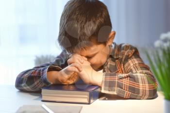 Little boy with Bible praying at home�