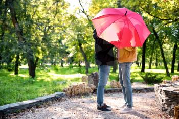 Happy gay couple with umbrella in park�