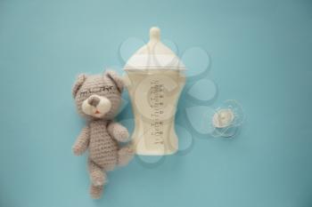 Feeding bottle of baby formula with pacifier and toy on color background�