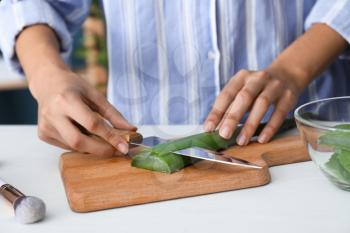 Woman cutting aloe leaf on wooden board�