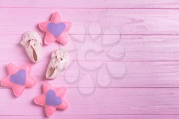 Baby shoes and toys on color wooden background, top view�