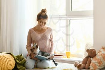 Woman with cute dog reading book at home�