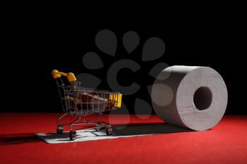 Roll of toilet paper and small shopping cart on table against dark background�