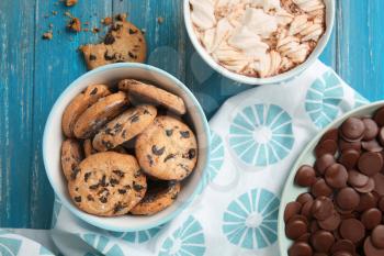 Tasty cookies with chocolate chips in bowl and cup of coffee on color wooden table�