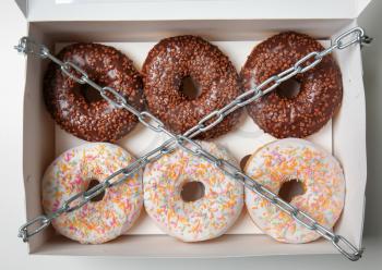 Tasty doughnuts with crossed chain in box. Concept of addiction�