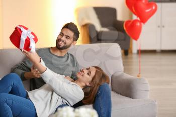 Young couple with gift box on sofa at home. Celebration of Saint Valentine's Day�