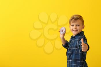 Cute little boy with donut showing thumb-up on color background�