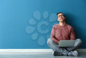 Young man with laptop sitting near color wall�