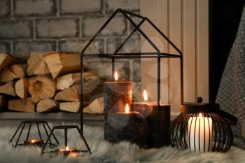 Beautiful burning candles on furry rug near fireplace�