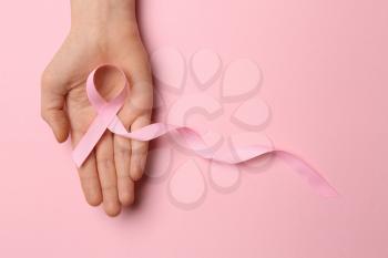 Female hand with pink ribbon on color background. Breast cancer awareness concept�