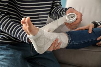 Man applying bandage onto his wife's leg at home�