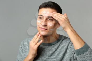 Portrait of young man with applied remedy for acne on grey background�