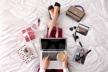 Young businesswoman with laptop drinking coffee on bed in morning�