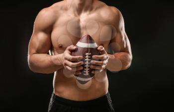 Muscular bodybuilder with rugby ball on dark background�