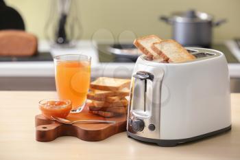 Toaster with bread slices and glass of juice on table�