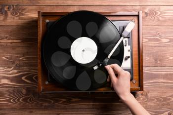 Woman switching on record player with vinyl disc on wooden background�