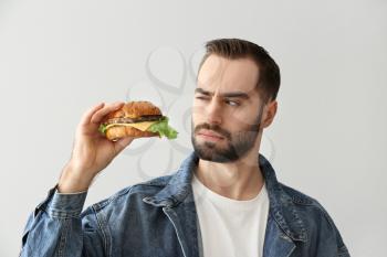 Suspicious man with tasty burger on light background�