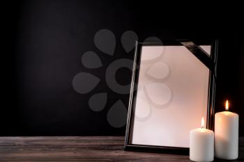 Blank funeral frame and candles on table against black background�