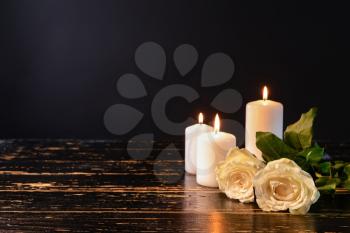Burning candles and flowers on table against black background�