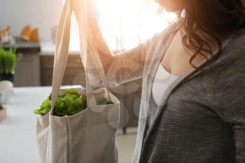 Young woman with fresh vegetables in eco bag indoors�