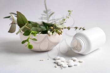 Bottle with pills and herbs on light background�