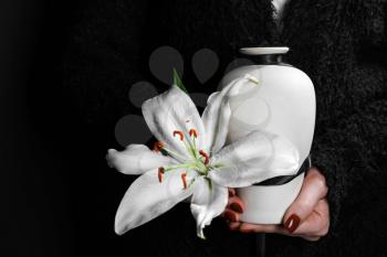 Woman holding mortuary urn with lily flower, closeup�