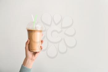 Female hand holding cup of tasty frappe coffee on light background�