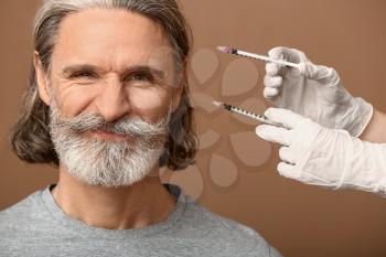 Mature man and hands holding syringes for anti-aging injections on color background�