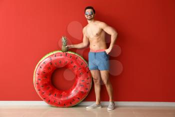 Handsome man with inflatable ring and pineapple near color wall�