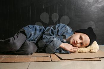 Homeless little girl lying on floor near dark wall�