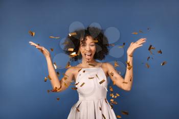 Happy African-American woman throwing confetti on color background�
