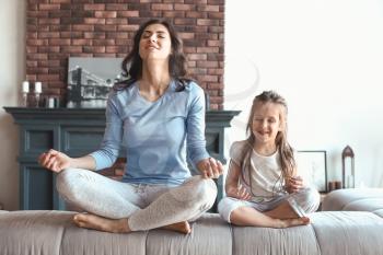 Mother with little daughter meditating at home�