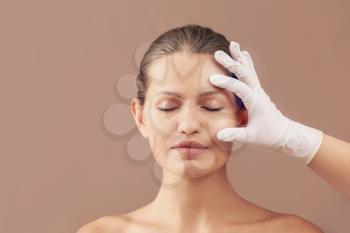 Plastic surgeon touching face of young woman on color background�