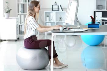 Young businesswoman sitting on fitball while working in office�