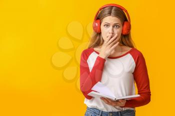 Shocked young woman listening to audiobook on color background�