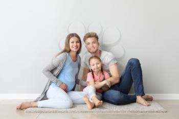 Beautiful pregnant woman with her family sitting near light wall�