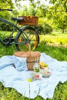 Bicycle and wicker basket with tasty food and drink for romantic picnic in park�